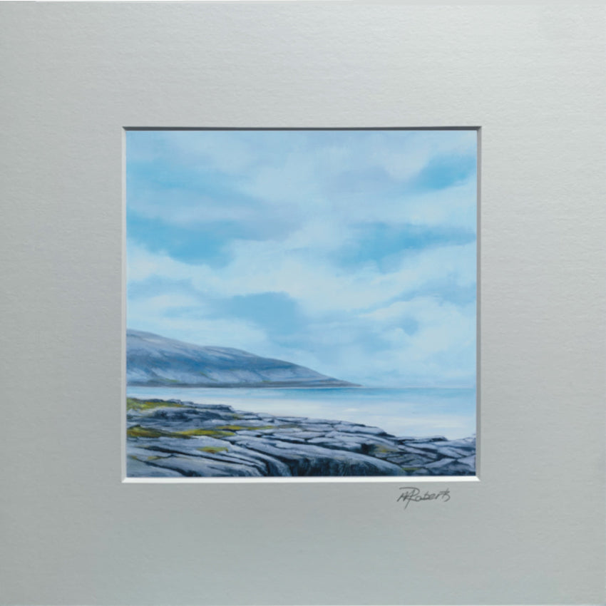 Framed artwork of a coastal landscape with a blue sky and rocky shore.